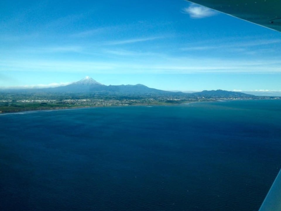 Aerial view of Mount Taranaki and the New Plymouth coastline, representing sustainability in New Zealand.
